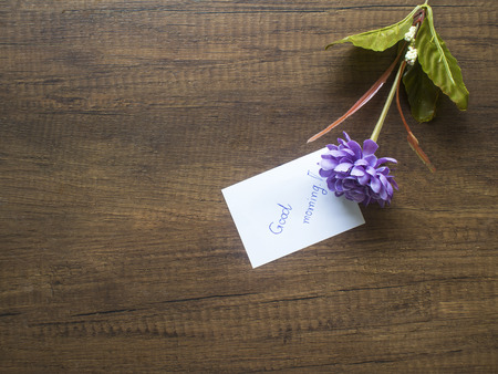 Flower and piece of paper with text "good morning" on the wooden table close-upの写真素材