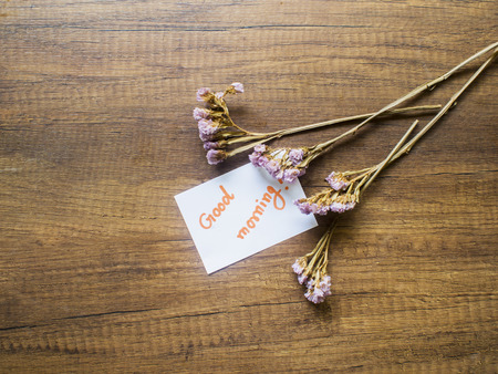 Flower and piece of paper with text "good morning" on the wooden table close-upの写真素材