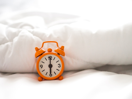 Alarm clock on bed in morning with sun lightの写真素材