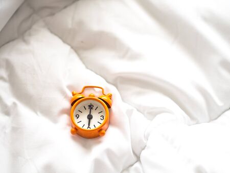 Alarm clock on bed in morning with sun lightの写真素材