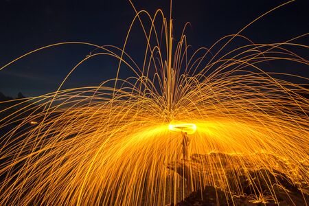 Showers of hot glowing sparks from spinning steel wool on the rock and beachの写真素材