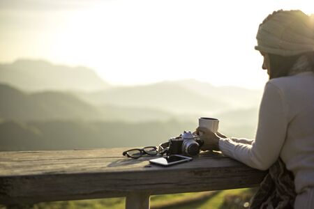 Woman drinking coffee in sun sitting outdoor in sunshine light enjoying her morning coffee, soft and select focusの写真素材