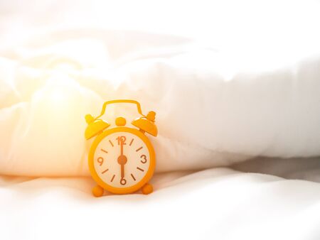 Alarm clock on bed in morning with sun lightの写真素材