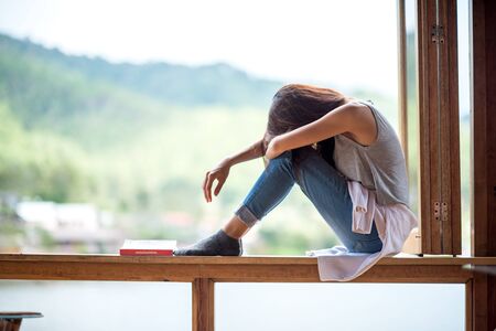 Young attractive woman, sitting on a window, lonely moodの写真素材