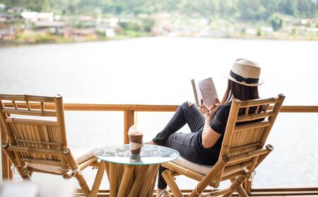 Woman reading a book lying and drink ice coffee on the chair,の写真素材