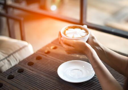 Hands holding hot cup of coffee or tea in morning sunlightの写真素材