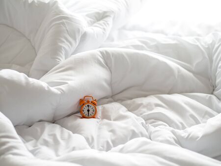 Alarm clock on bed in morning with sun lightの写真素材