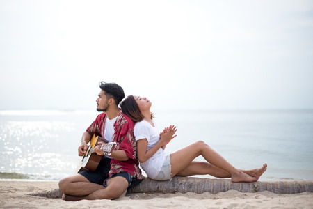 Cute hispanic couple playing guitar serenading on beach in love and embraceの写真素材