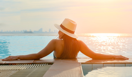 Young woman in big hat relaxing on the swimming pool, near the sea in the sunsetの写真素材