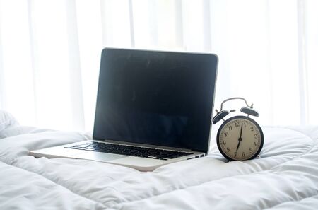 The laptop and alarm clock in the morning on a white bed, soft and select focusの写真素材