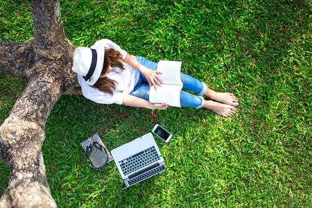 Girl enjoy listening music and playing laptop on the grass field of the park in the morningの写真素材