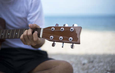 Close up handsome man playing classic guitar sitting on the beach in vacationsの写真素材