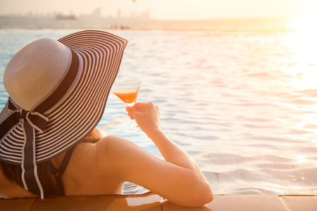 Young woman in big hat relaxing on the swimming pool, near the sea in the sunsetの写真素材