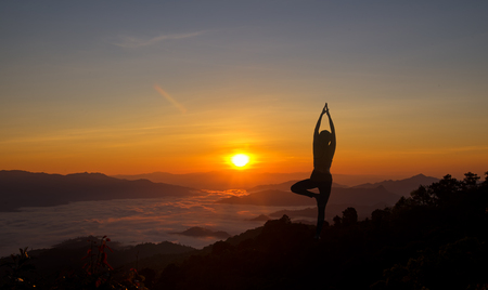 Silhouette young woman practicing yoga on the mountain at sunrise morningの写真素材