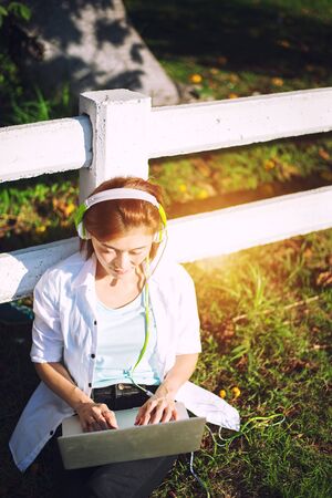 Young women relaxation listening music with notebook sitting on the grass. Outdoor. Sunny day.Greeney tone 2017

の写真素材