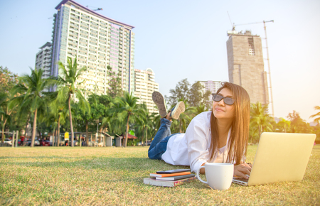Women work in the park with the laptop and coffee, relax work, background cityの写真素材