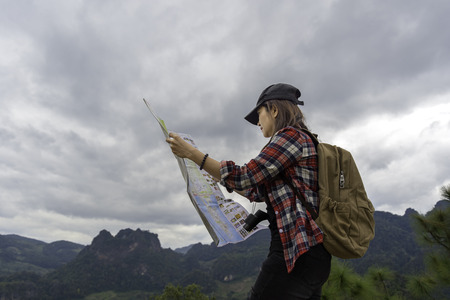 Women traveler with backpack checks map to find directions in wilderness areaの写真素材