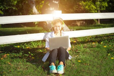 Young women lying in summer grass with headphones listening to music and playing laptop, sunny day, greenery 2017の写真素材