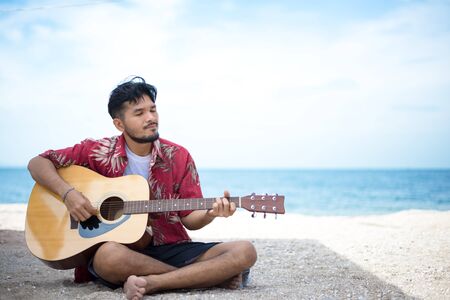 Handsome man playing classic guitar sitting on the beach in vacationsの写真素材
