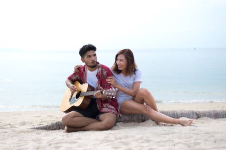 Cute hispanic couple playing guitar serenading on beach in love and embraceの写真素材