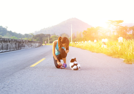 Puppy dog and young women running exercise on the street park in the morning. Young woman teaching her puppy dog obedience gesturing with her finger for it to sit or stayの写真素材