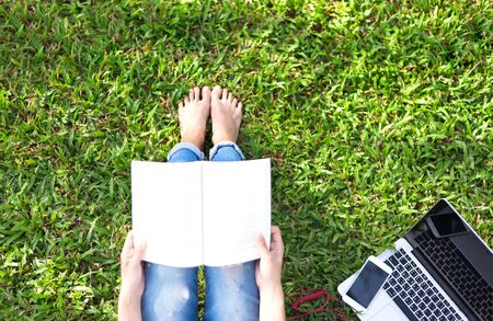 Girl enjoy listening music and reading a book and play laptop on the grass field of the park in the morningの写真素材