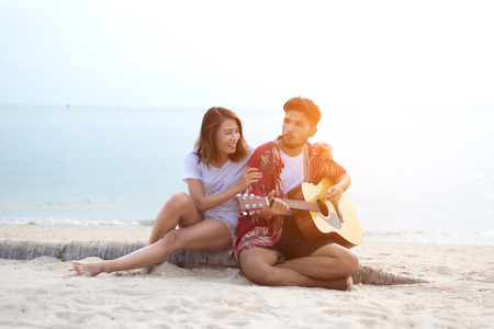 Cute hispanic couple playing guitar serenading on beach in love and embraceの写真素材