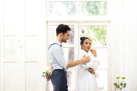 Young man trying to reconcile his girlfriend offering white rose in the white roomの写真素材