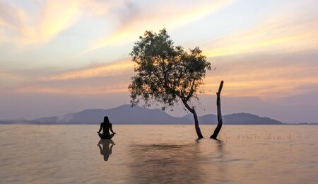 Silhouette of woman sitting on the lake during a beautiful sunset, with reflection in the water.の写真素材
