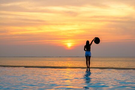 Woman holding hat relaxing at the pool on the sunset and twilightの写真素材