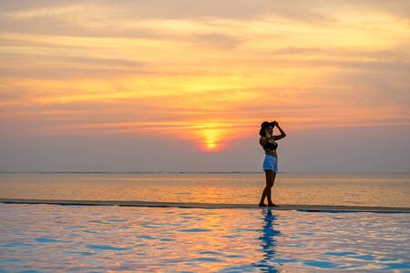 Woman holding hat relaxing at the pool on the sunset and twilightの写真素材