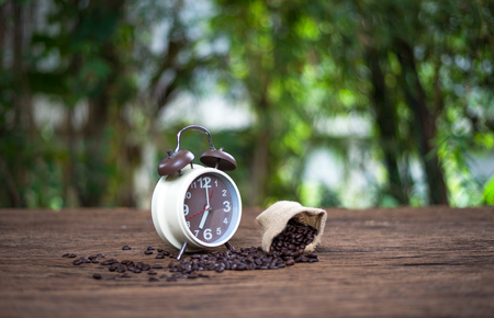 Alarm clock with coffee beans on wooden table with morning light, Start up conceptの写真素材