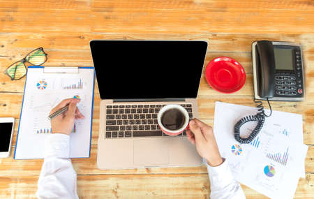 Fresh coffee for great ideas. Top view ofman working on laptop and holding cup of coffee while sitting at his working placeの写真素材
