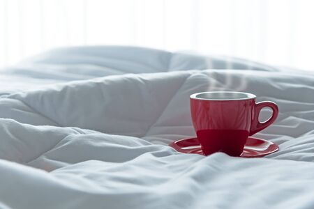 Fresh morning coffee in red cup on the bed.の写真素材
