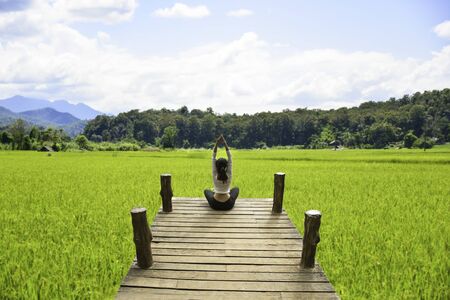 Healthy woman practicing yoga on the bridge in the nature, background rice fieldの写真素材