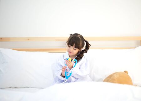 Cute kid girl playing doctor with plush toy at homeの写真素材