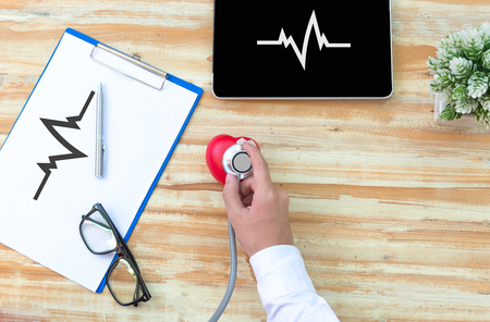 The doctore with a medical stethoscope check heart near a laptop on a wooden tableの写真素材