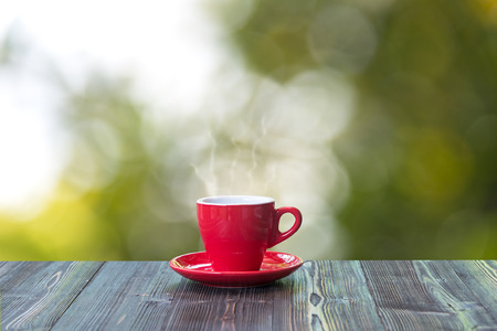 Hot coffee with in red cup on wood table and nature bokeh backgroundの写真素材