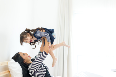 Happy family mother and child daughter play and laugh in bedの写真素材