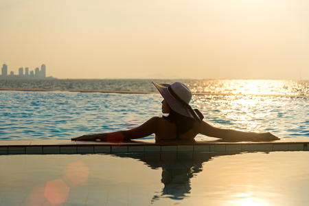 Woman in big hat relaxing on the swimming pool, near the sea in the sunsetの写真素材