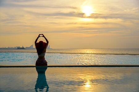 Woman in big hat relaxing on the swimming pool, near the sea in the sunsetの写真素材