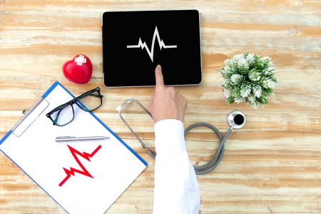 The doctor with a medical stethoscope check heart near a laptop on a wooden tableの写真素材