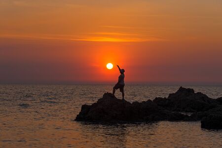 Silhouette of man with their hands in the sunset on the oceanの写真素材