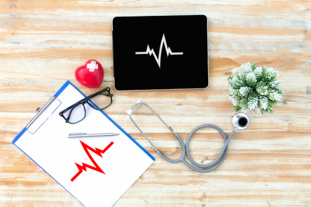 The doctor with a medical stethoscope check heart near a laptop on a wooden tableの写真素材