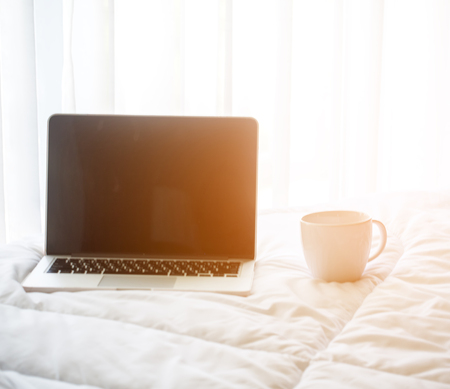 The laptop and coffee in the morning on a white bed, soft and select focusの写真素材