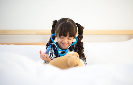 Cute kid girl playing doctor with plush toy at homeの写真素材