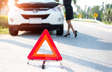 Business woman with a broken car calling for assistance. Focus is on the red triangle signの写真素材