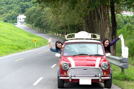 Two travel woman in car road trip waving out the window smilingの写真素材