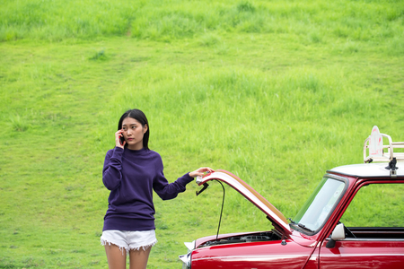 Young woman using mobile phone while looking at broken down car on streetの写真素材