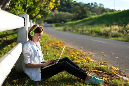 Young women relaxation listening music with notebook sitting on the grass. Outdoor. Sunny day.の写真素材